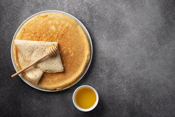 stack of pancakes on a plate with honey on a dark gray background, top view,maslenitsa