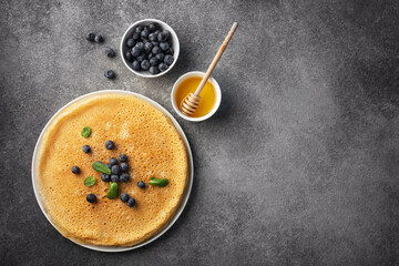 stack of pancakes on a plate with blueberries and mint leaves, honey on a dark gray background, top view, maslenitsa