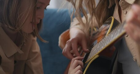 preschooler girl is looking how her mother playing guitar and touching strings, curiosity and fun