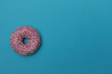 rosa Donut mit Zuckerguss und Zuckerstreuseln auf blauem Untergrund - Single pink donut with icing and sugar sprinkles on a blue background