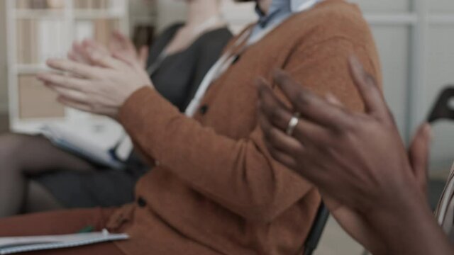 Racking focus of cropped unrecognizable business people sitting in conference room, and clapping hands