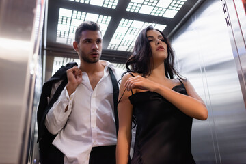 Brunette woman taking off dress near boyfriend in formal wear in elevator