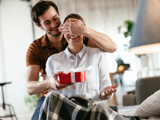 Husband surprising his wife with a gift. Young man giving a gift box to his wife..