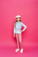 girl in fashionable clothes smiling at camera while posing with hand on hip on pink