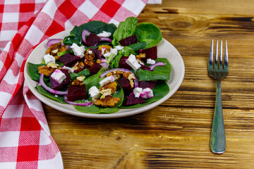Tasty spinach salad with boiled beetroot, feta cheese, walnut and red onion on wooden table. Healthy vegetarian food