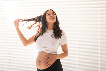 Smiling young beautiful pregnant woman touching her belly and hair and rejoicing. Concept of health and thinking about the future while waiting for baby. Copyspace