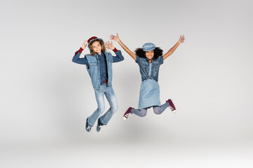 full length view of excited multicultural girls in trendy clothes levitating on grey