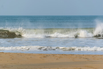 Panoramic landscape view of large foamy sea wave from Arabian Sea splashing with spray of water droplets in the air at Gokarna situated on the West Coast, Karnataka, India.
