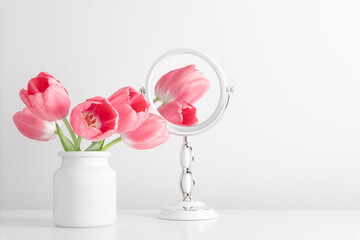 Pink tulips in vase and reflection of flowers in mirror. Spring flowers in the bathroom shelf....