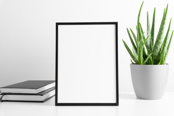 Black frame mockup with workspace accessories and aloe vera on white table. Front view. Place for text, copy space, mockup