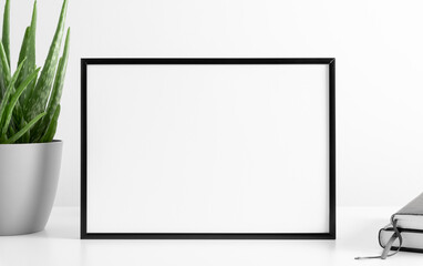 Black frame mockup with workspace accessories and aloe vera on white table. Front view. Place for...