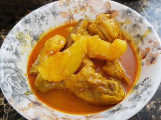 Traditional Malaysian Malay chicken curry is served on a white flowered plate. The dish is gravy and topped with large chopped potatoes. 