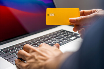 Tarjeta de crédito o débito amarilla sujetada por una mano frente a un ordeandor portátil...