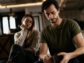 Young man checking empty wallet, no money. Unemployed sad man sitting at home with wife showing empty wallet