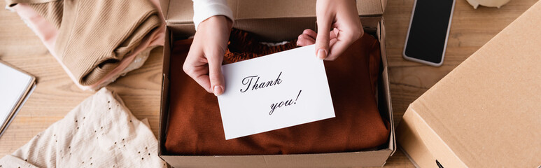Partial view of proprietor holding card with thank you lettering near box with clothes, banner