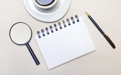 On a light gray background, a white cup with coffee, a magnifying glass, a pen and a blank notebook with a place to insert text or illustrations. Template. Top view with copy space