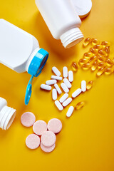 Flat lay of pills, fish oil, vitamins with green leavws on yellow background