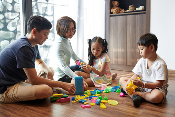Vietnamese parents and children sittig on floor in living room and playing with plastic toys and blocks