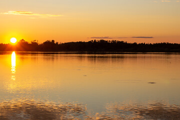 A colorful sunny sunset is reflected on the surface of the calm lake.