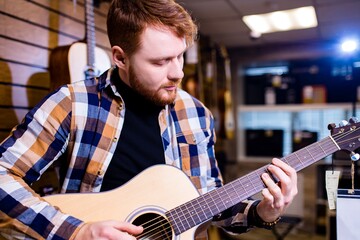 Man with red ginger hair and beatd is considering a guitars in a music store