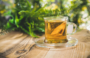 Glass tea cup with bag on wooden table in front of blurred nature background of flovers and leaves. Bokeh concept