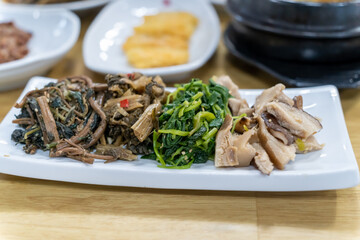 In Korean cuisine, side dishes such as seasoned vegetables are served on a white plate.