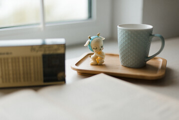 a mug and a figurine on a tray against the background of a window