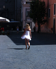 A beautiful girl with her back turned with a model figure harry up forward  around the city in a white dress fluttering in the wind