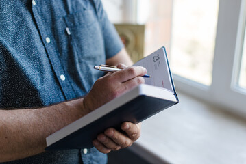 a man in a blue shirt writes in a notebook with a pen