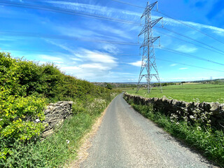 Obraz premium Looking along, Deep Lane, with dry stone walls, fields and pylons, on a sunny day near, Bradford, Yorkshire, UK