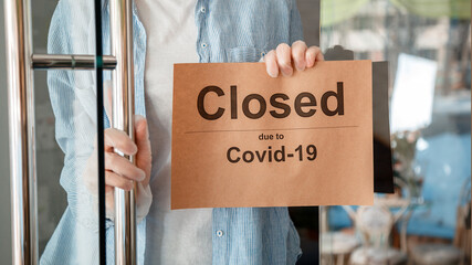 Sign Closed covid 19 lockdown on shop entrance door as new normal shutdown. Unrecognizable Woman in...