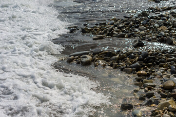 pebble stones on the sea beach, the rolling waves of the sea with foam