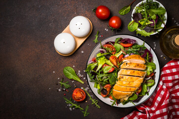 Fresh salad with baked chicken breast at dark kitchen table. Top view with copy space.