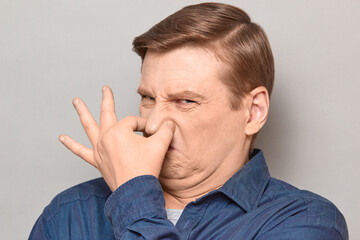 Portrait of mature man pinching his nose and grimacing from disgust