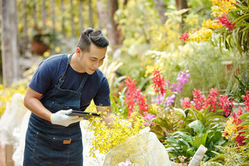 Happy male flower nursery worker with digital tablet unwrapping plants covered wigh nonwoven material