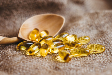Fish oil capsules in a wooden spoon. Fish oil pills, tablets on the burlap. Vitamin complex omega...