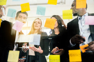 Group of successful business teamwork. Brainstorm meeting with colorful sticky paper note on glass wall for new ideas. Using agile methodology and do business. Brainstorming in a tech start-up office.