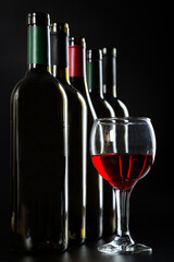 several different bottles of wine and a glass with red wine on a dark glossy background.