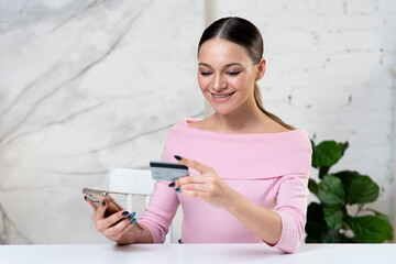 Young happy girl, positive woman looking at credit bank card paying online in shop, enter information, shopping, order in internet store, doing secure payment on cell mobile phone, smartphone, smile