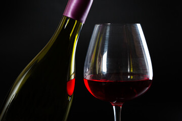 Wine bottle and glass with red wine on dark glossy background.