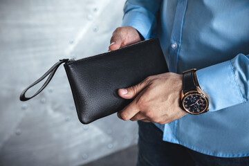 A business man in the interior holds a leather black clutch in his hands. No face, horizontal orientation - obrazy, fototapety, plakaty