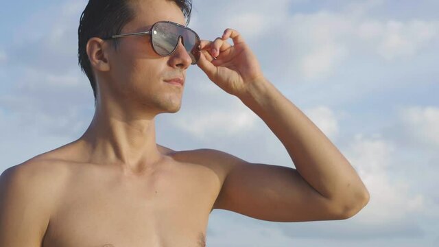Portrait of smiling topless man wearing sunglasses and looking forward. summer time with blue sky