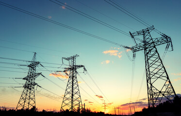 silhouette of high voltage power lines against a colorful sky at sunrise.