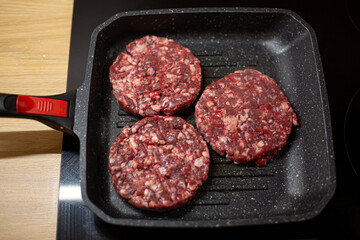 Burger raw minced beef meat cutlet on a grill pan. Process of cooking self made burgers at home