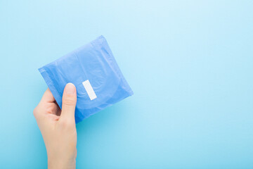 Young adult woman hand holding pack of sanitary towel on light blue table background. Pastel color....