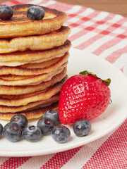 Close-up of delicious pancakes, with fresh blueberries, strawberries and maple syrup on a light background. With space to copy. Sweet maple syrup flows from a stack of pancakes
