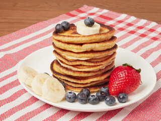 Close-up of delicious pancakes, with fresh blueberries, strawberries and maple syrup on a light background. With space to copy. Sweet maple syrup flows from a stack of pancakes