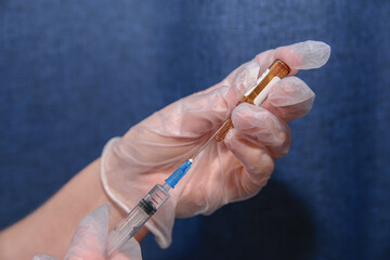 Ampoule of medicine and syringe in hands with clear medical gloves