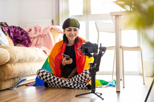 Gender fluid person wrapped in rainbow flag filming a vlog with camera