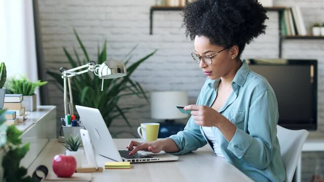 Video of pretty young afro woman shopping online with credit card with laptop while working on office at home.